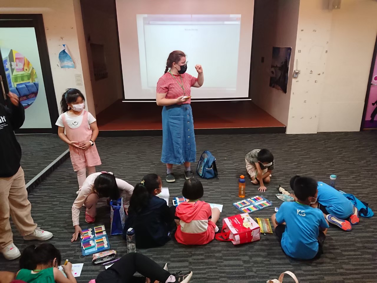 Gretchen standing in front of circle of children sitting on the floor working